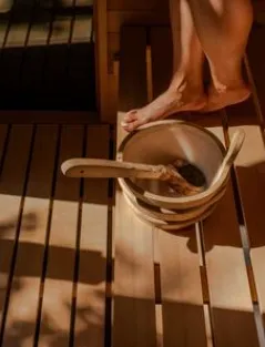 A wooden bucket and ladle on sunlit sauna benches